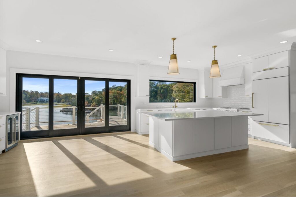 Open-concept kitchen with white cabinetry, brass pendants, and tidal cove views inside a Cohasset, MA custom home by Oak.